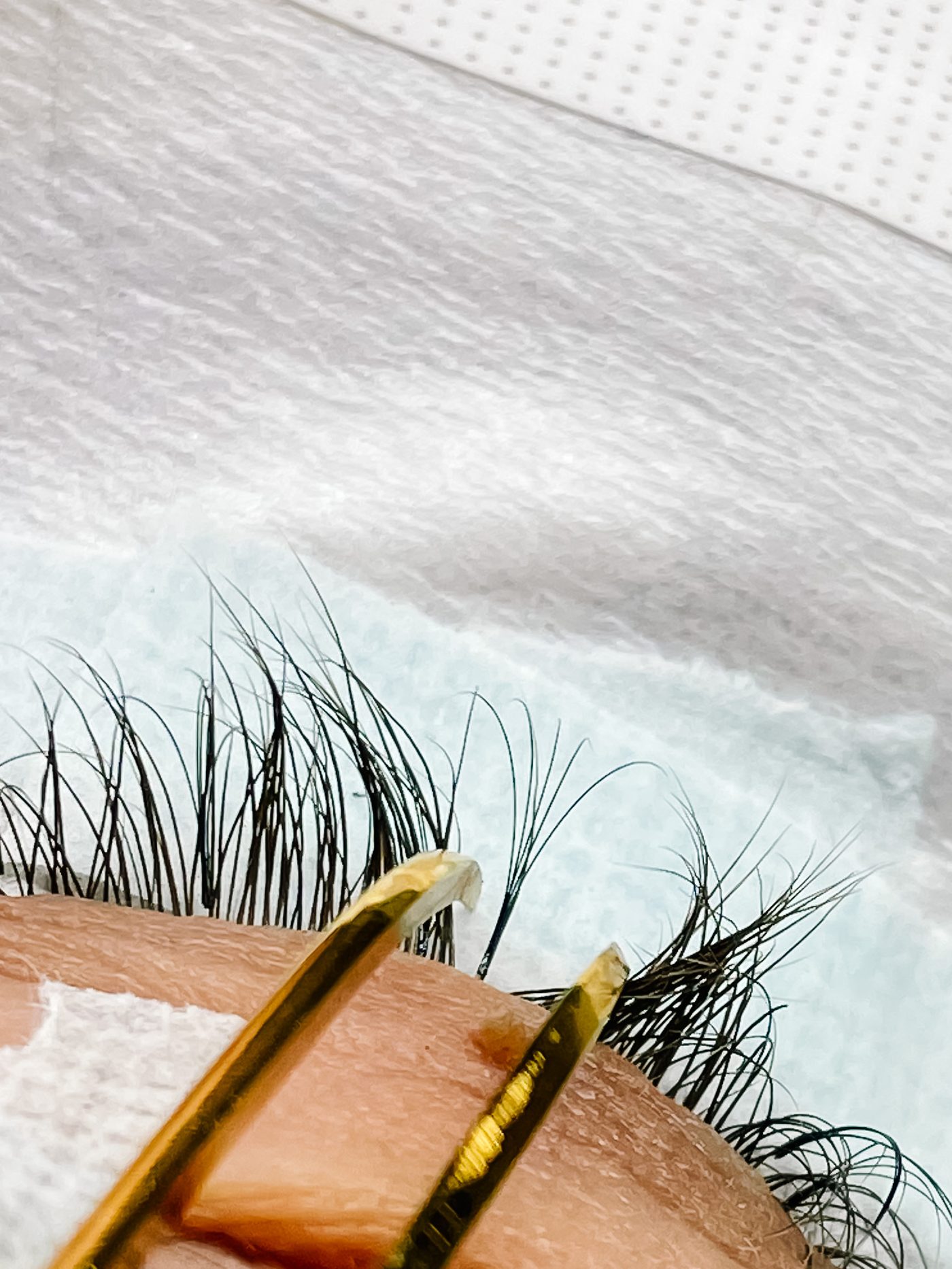 Handmade lash fans on a tile beside gold tweezers