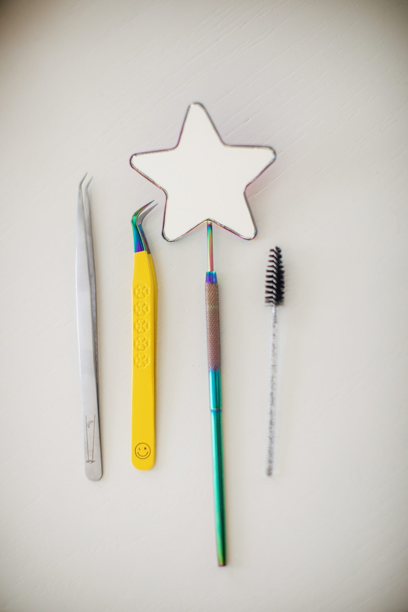 Lash tools laid out: isolation tweezers, volume tweezers, spoolie and lash tile